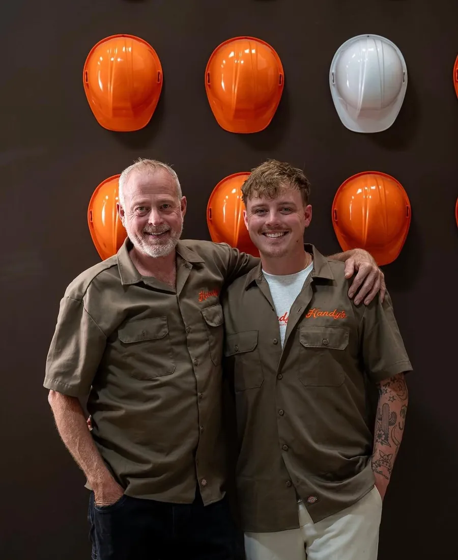 Peter Leary and Tim Leary of Handy's in uniform, in front of a wall of orange hard hats