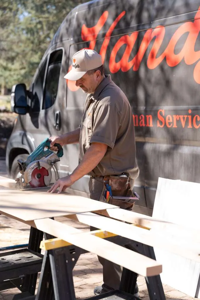 A Handy's technician cutting wood with a circular saw in front of the Handy's van