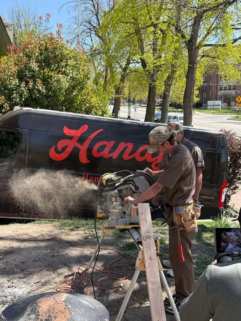 A Handy's technician cutting a board with a mitre saw beside a Handy's van