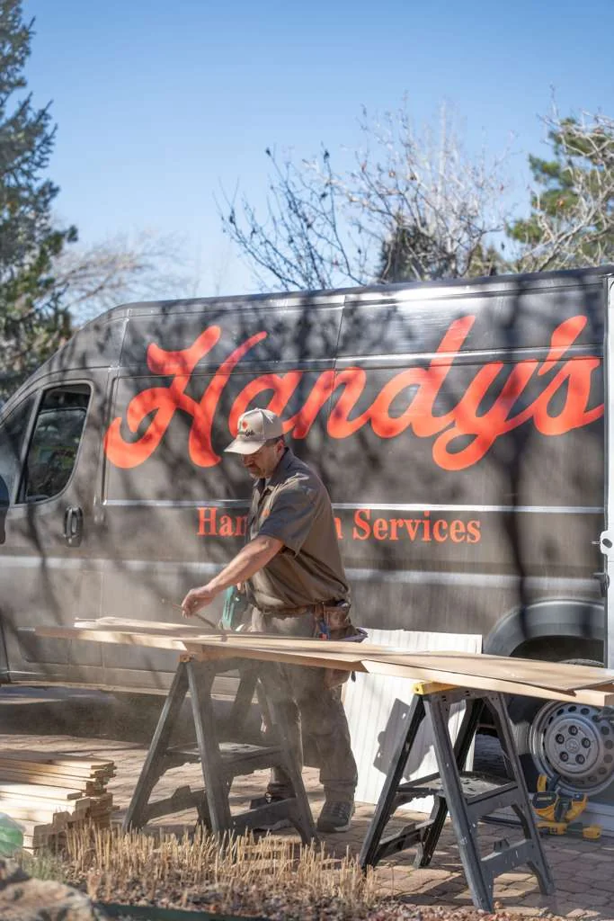 A Handy's technician cutting boards on sawhorses beside the van