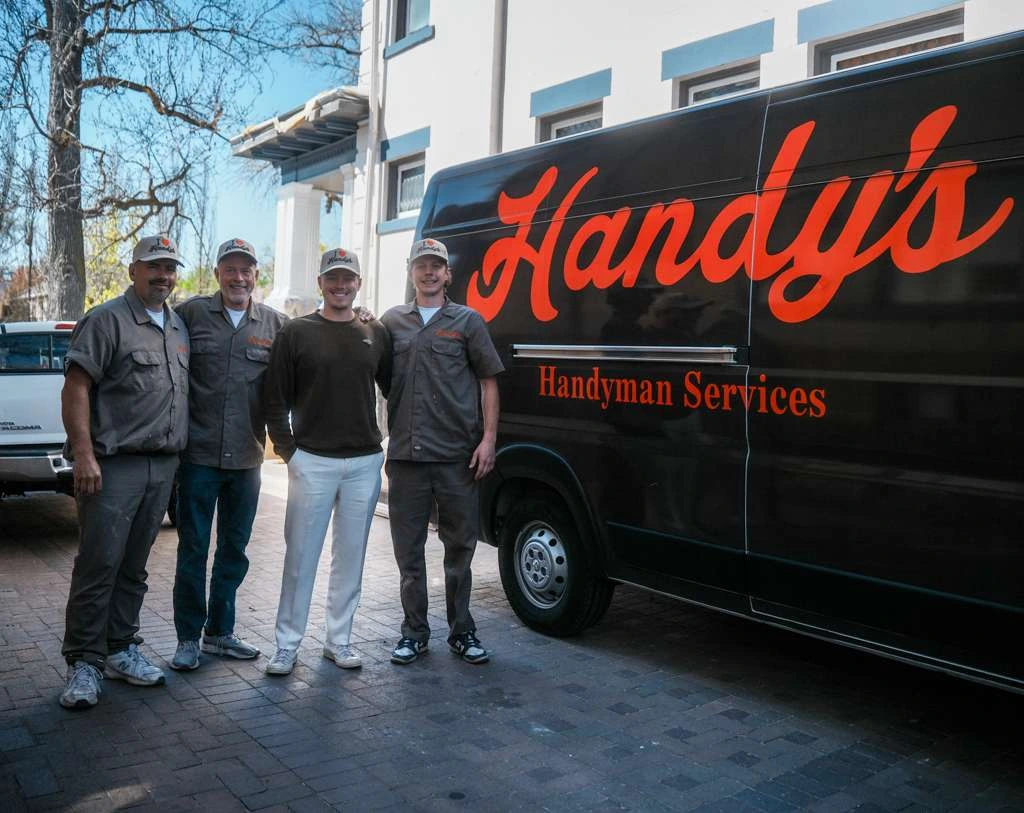 Four members of the Handy's team in Handy's caps, standing in front of a Handy's van